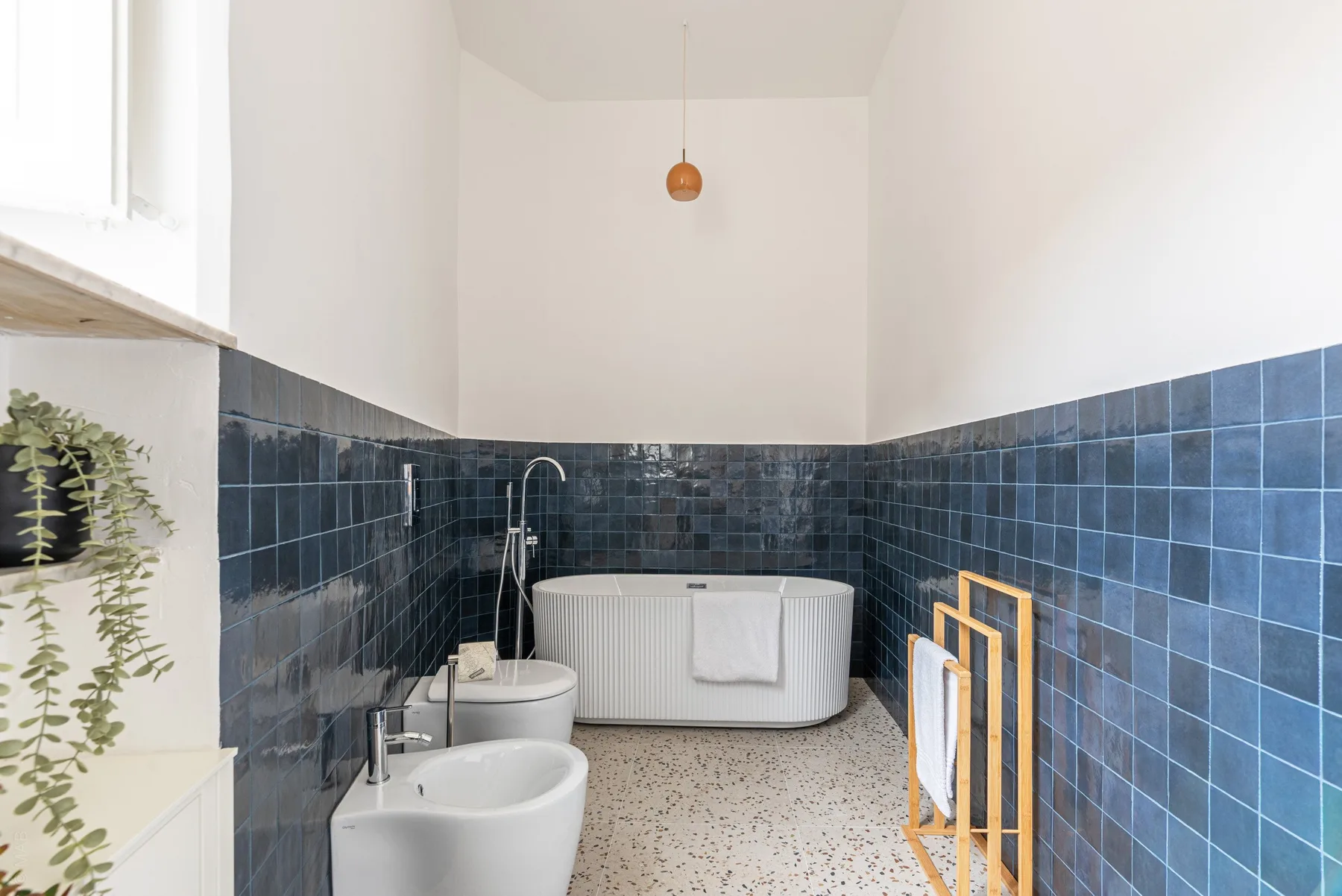 A bathroom with a bathtub and dark blue tiled walls.