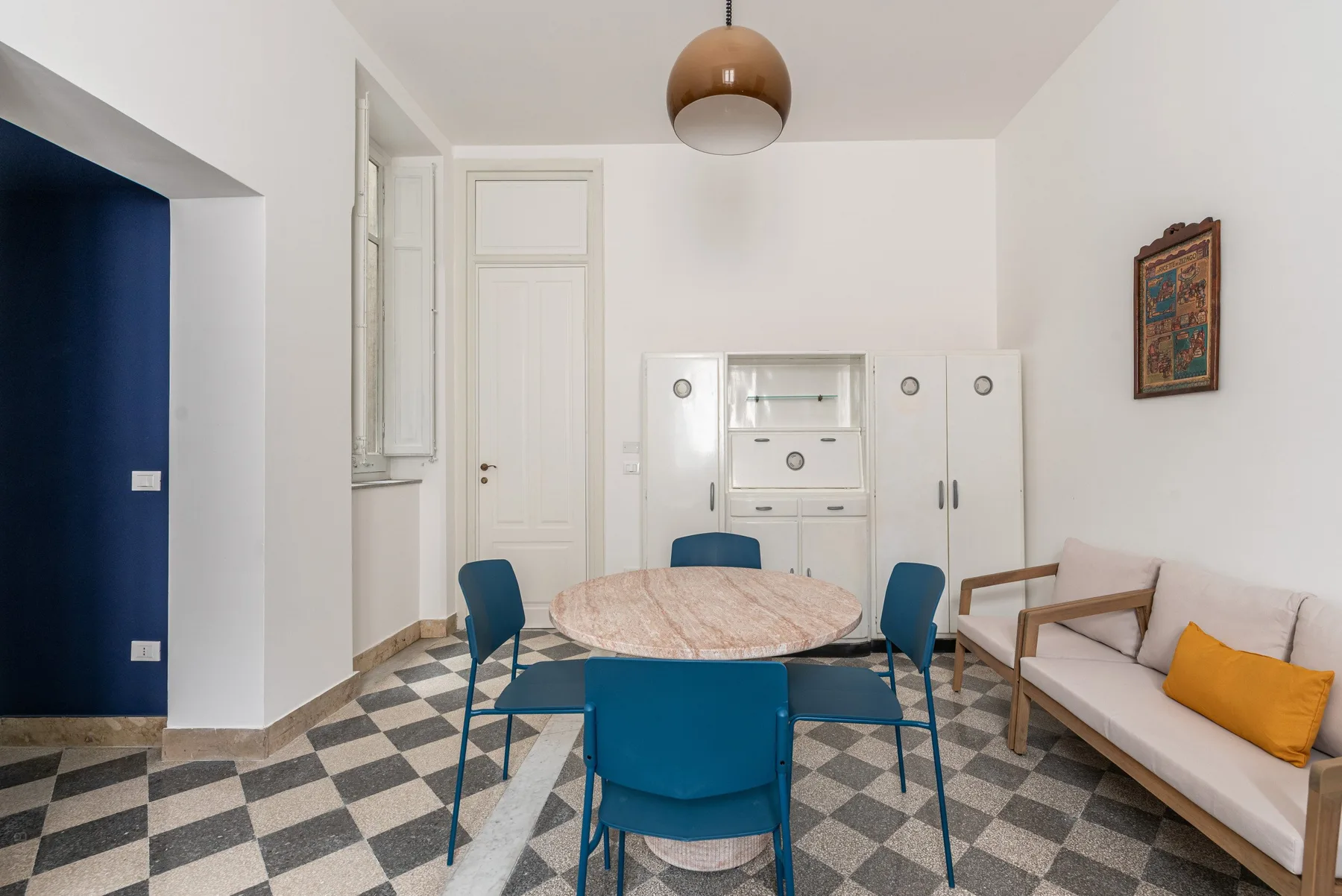 A dining area with a round table and blue seating beside a sofa.