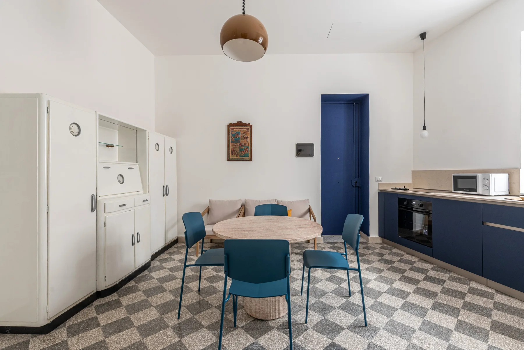 A bright kitchen dining area has a round table, blue seating, and built-in cabinets.