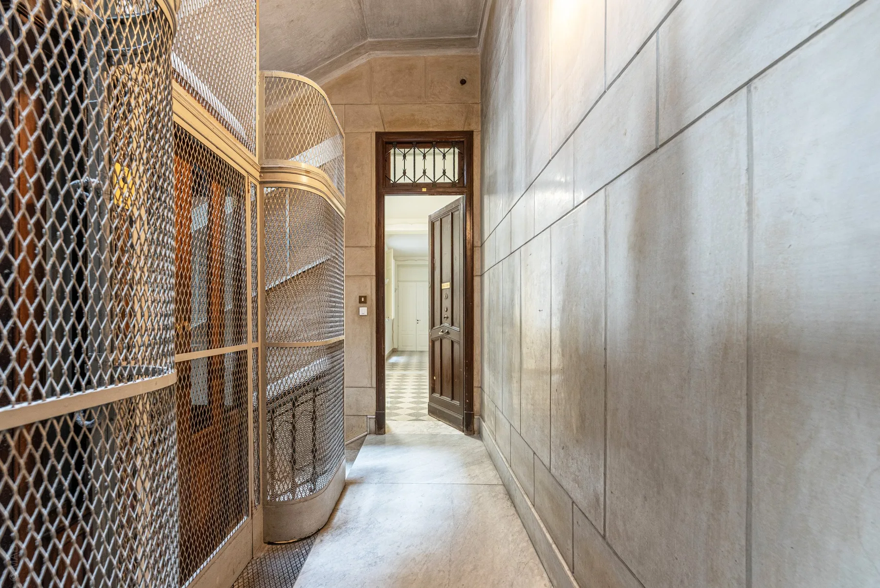 A narrow stone corridor with metal mesh partitions and an open doorway.