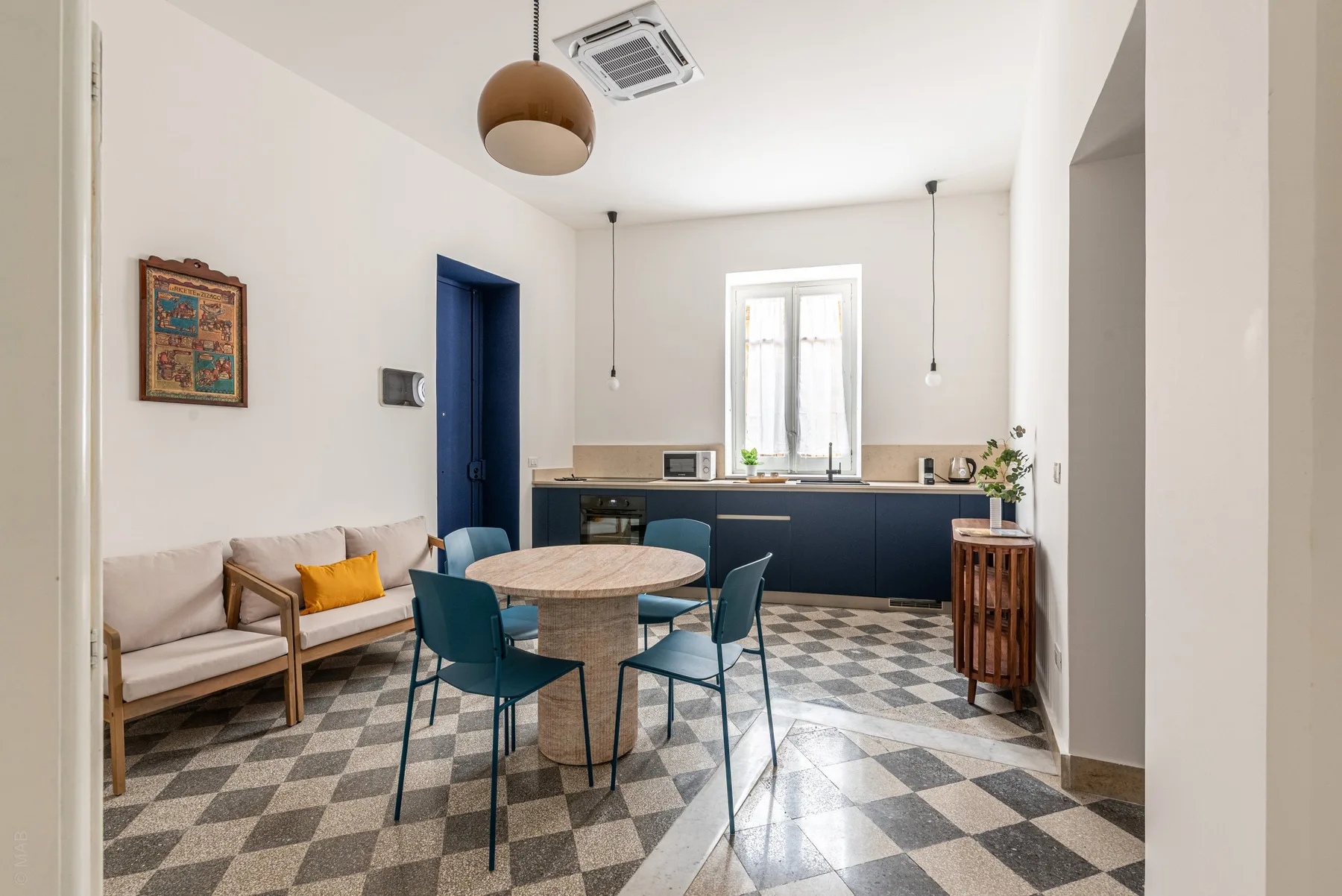 A dining area with a round table and seating opens onto a kitchen with dark cabinets.