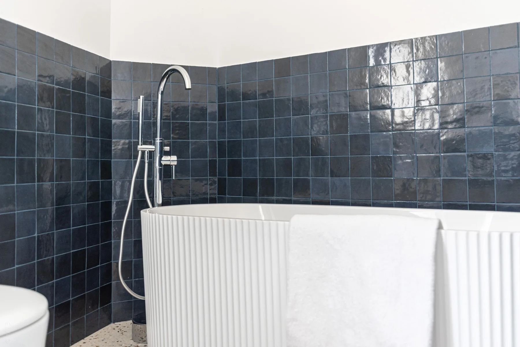 A bathroom with a white bathtub and dark tiled walls.