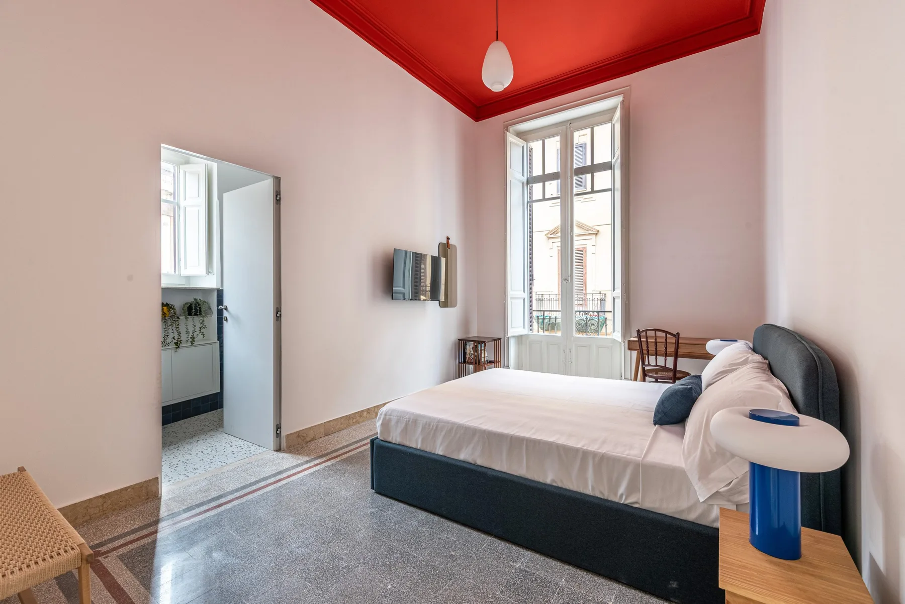 A bedroom with a bed, tall windows, and a vivid red ceiling.