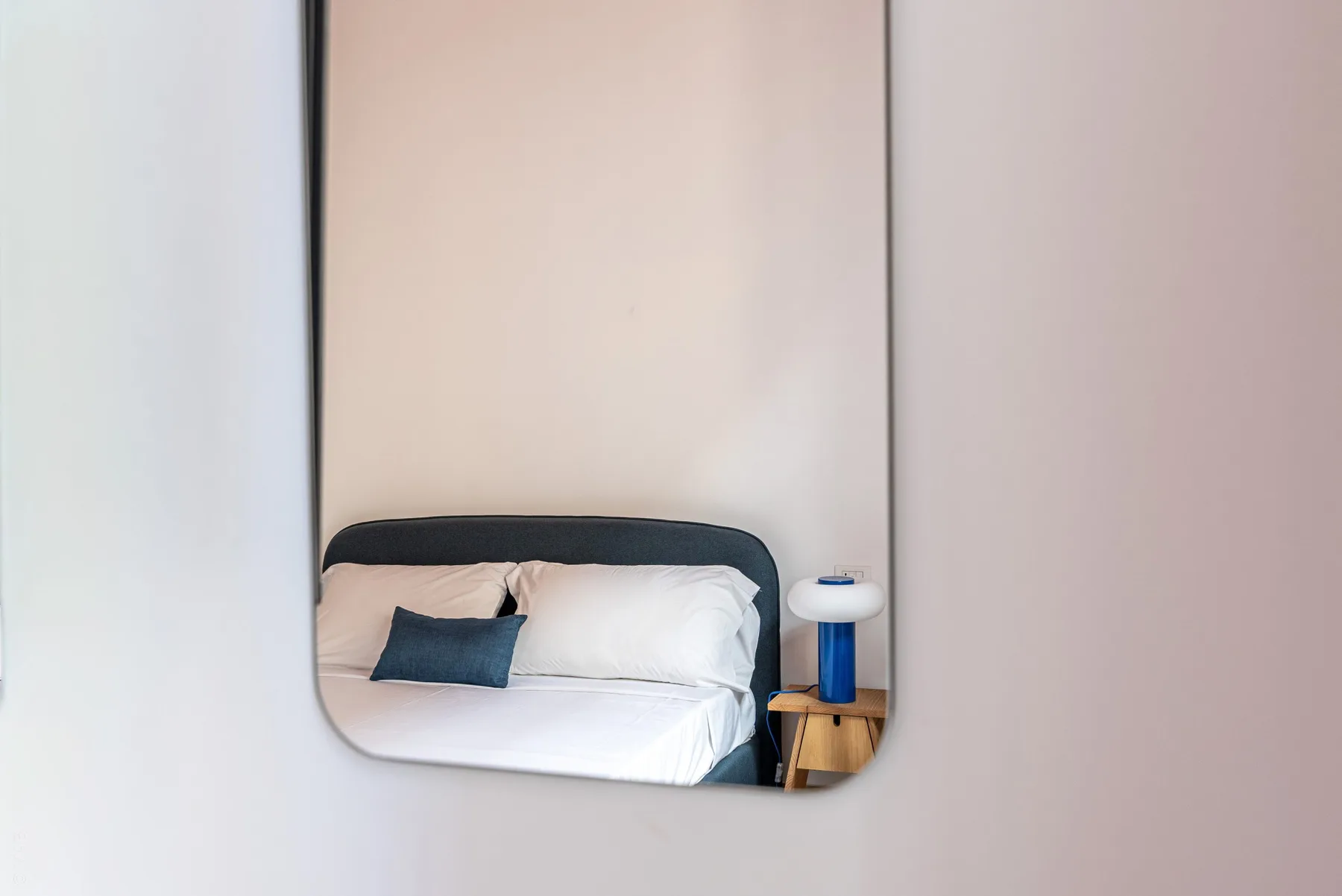 A bedroom with a bed and a small bedside table, seen in a mirror.