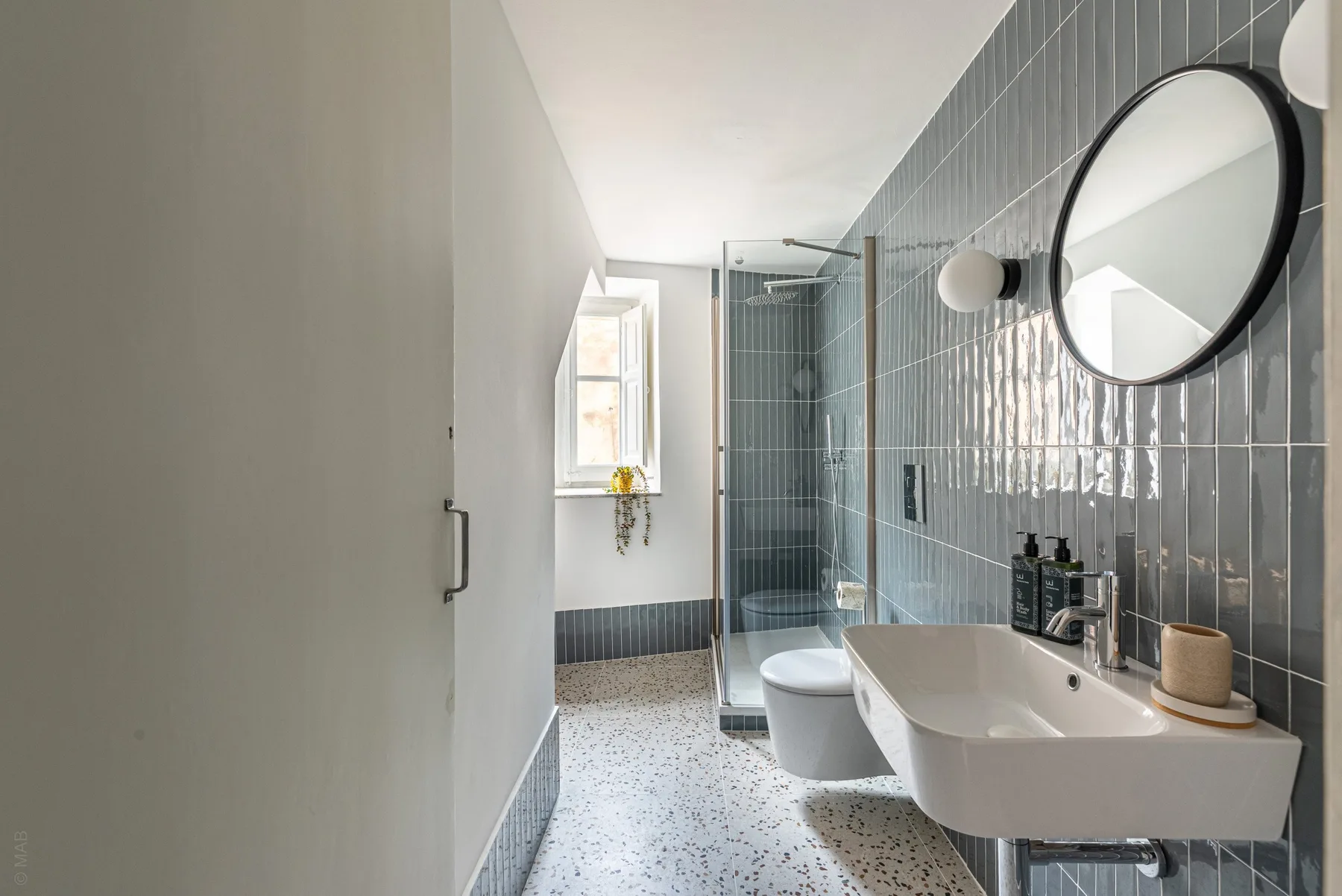 A bright bathroom with a glass shower, wall-mounted toilet, and sink.