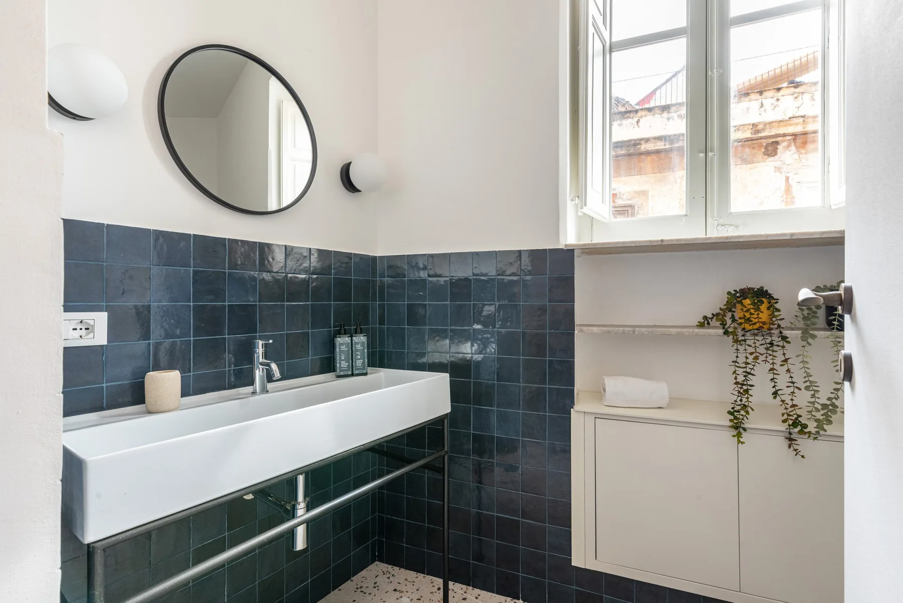 A bathroom with a long white sink beneath a round mirror.