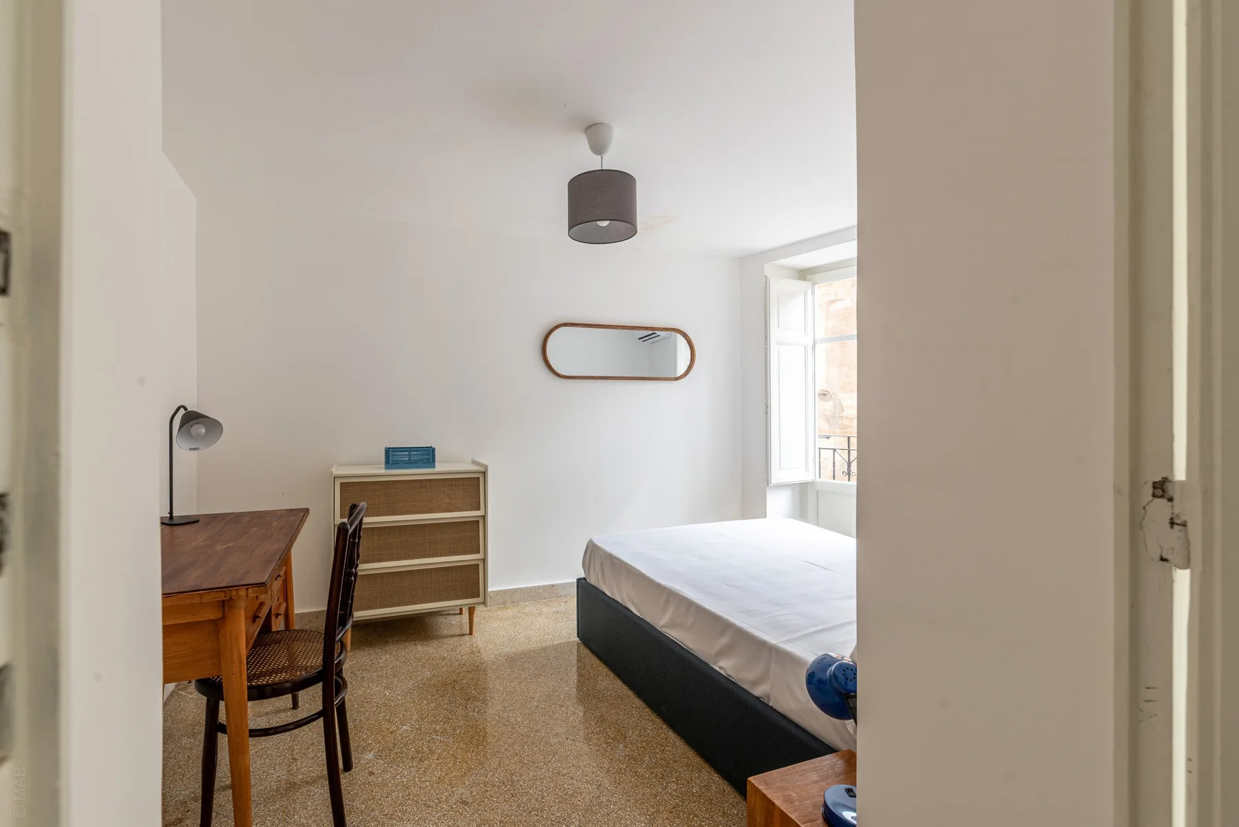 A bright bedroom with a bed, a desk, and a window.