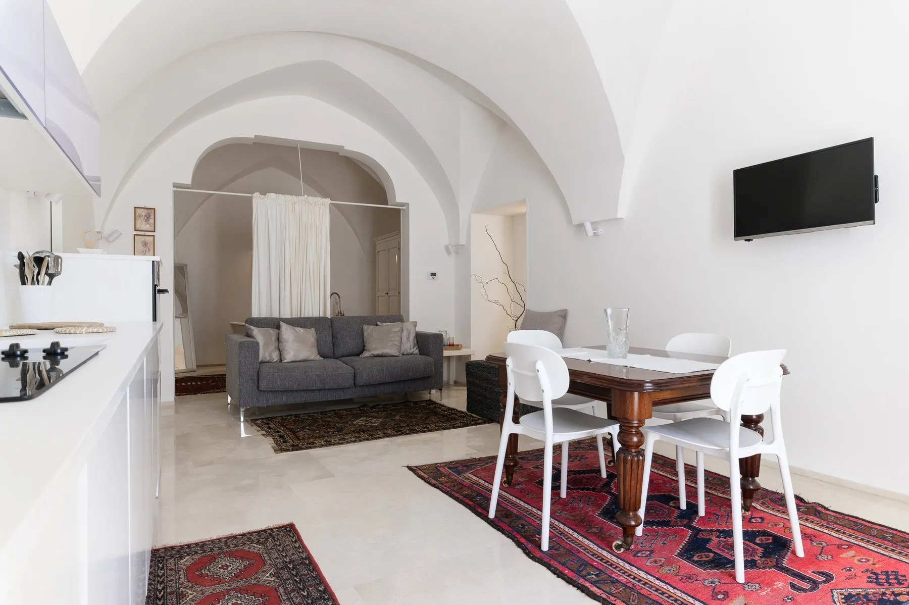 A bright living and dining area has arched ceilings, seating, and a dining table.