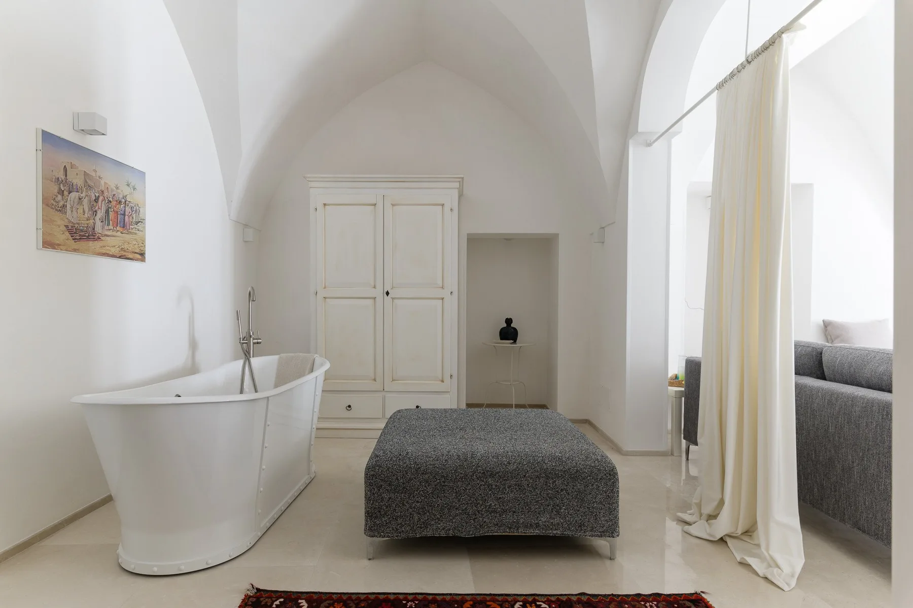 A bright bedroom features a freestanding bathtub and a gray upholstered bed.