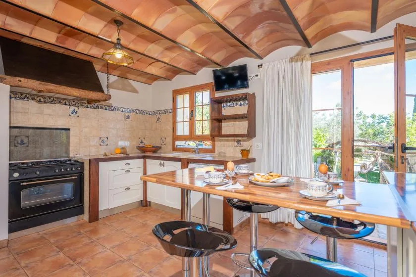 Una cocina y comedor con una mesa larga junto a puertas de vidrio abiertas.