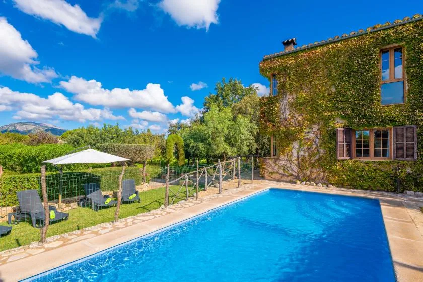 Una piscina exterior junto a un edificio cubierto de hiedra y un jardín.