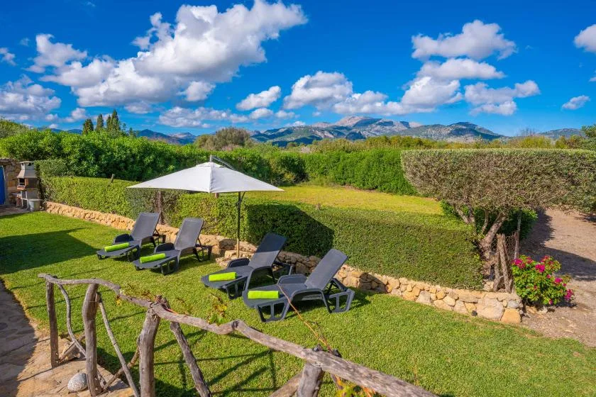 Una zona de jardín con tumbonas reclinables, una sombrilla blanca y vistas a las montañas.