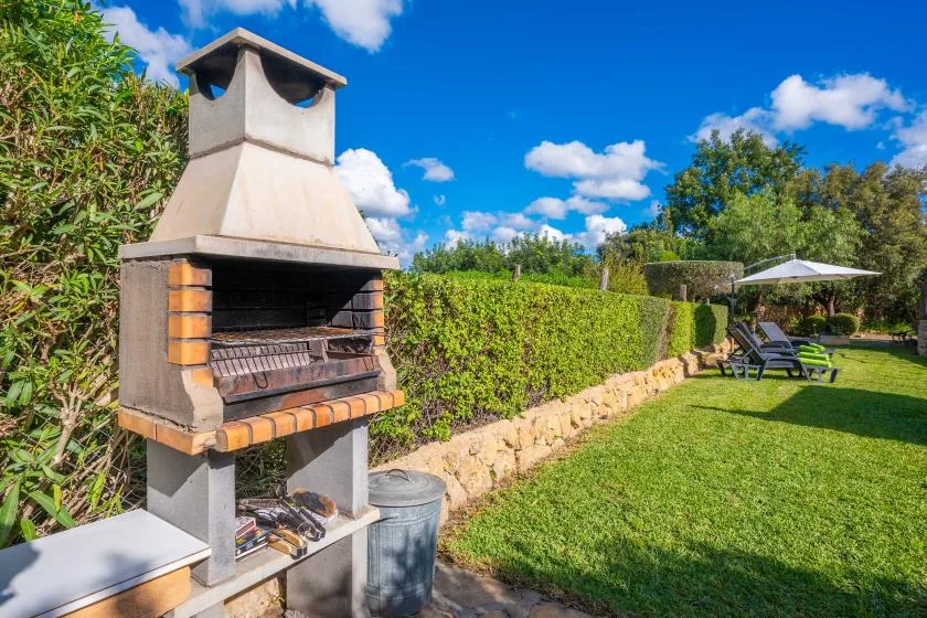 Un patio ajardinado con una barbacoa exterior junto a un seto y césped.