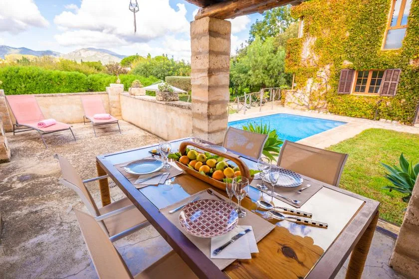 Una zona de comedor al aire libre da a una piscina y un jardín frondoso.