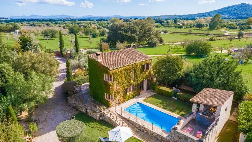 Una villa rural y una piscina se encuentran entre campos verdes y árboles.