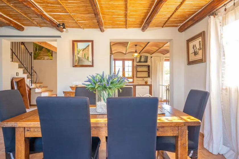 Comedor con una mesa de madera y asientos tapizados en azul bajo un techo de vigas de madera.