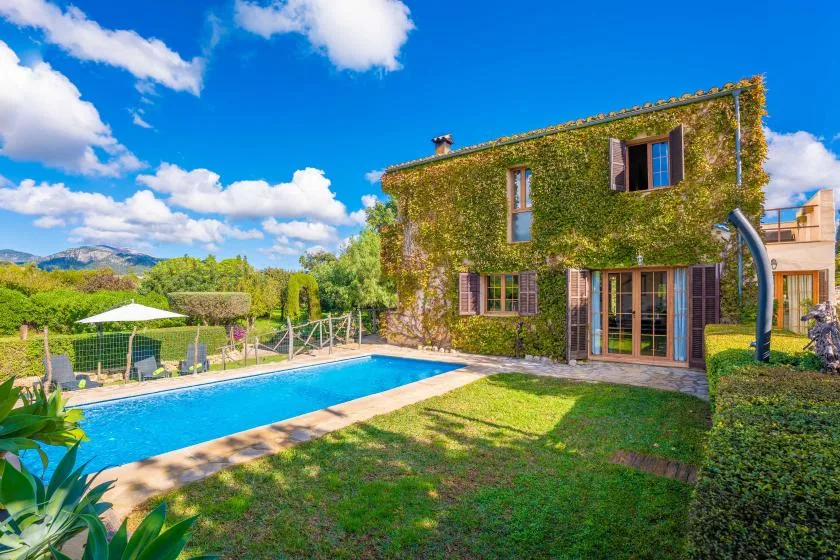 Una casa cubierta de enredaderas está junto a una piscina y un césped verde.
