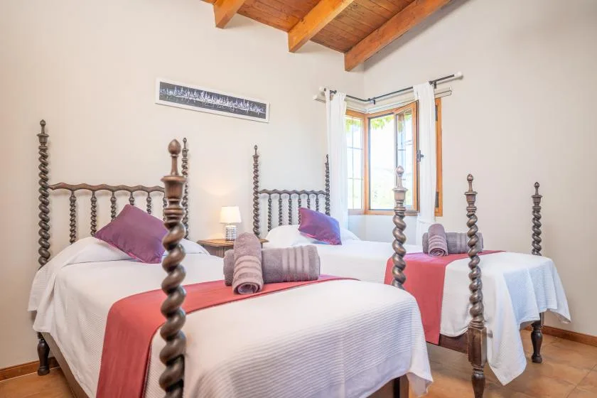 Un dormitorio luminoso con varias camas, caminos de colores y una ventana.
