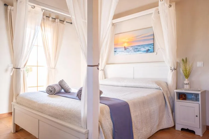Un dormitorio con una cama con dosel, cortinas translúcidas y una imagen de playa sobre el cabecero.