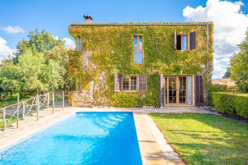 Una casa cubierta de hiedra se encuentra junto a una piscina y un jardín con césped.