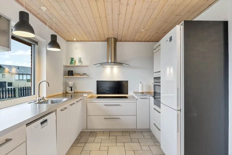 Una cocina luminosa con gabinetes blancos, una estufa central y una ventana grande.