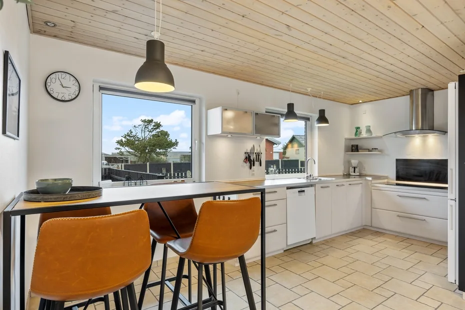 Una cocina luminosa con gabinetes blancos, una isla central y asientos de barra.