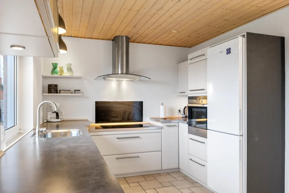 Una cocina moderna con gabinetes blancos, una encimera larga y una zona de cocción central.