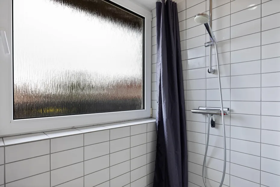 Una ducha de baño alicatada junto a una ventana esmerilada y una cortina oscura.