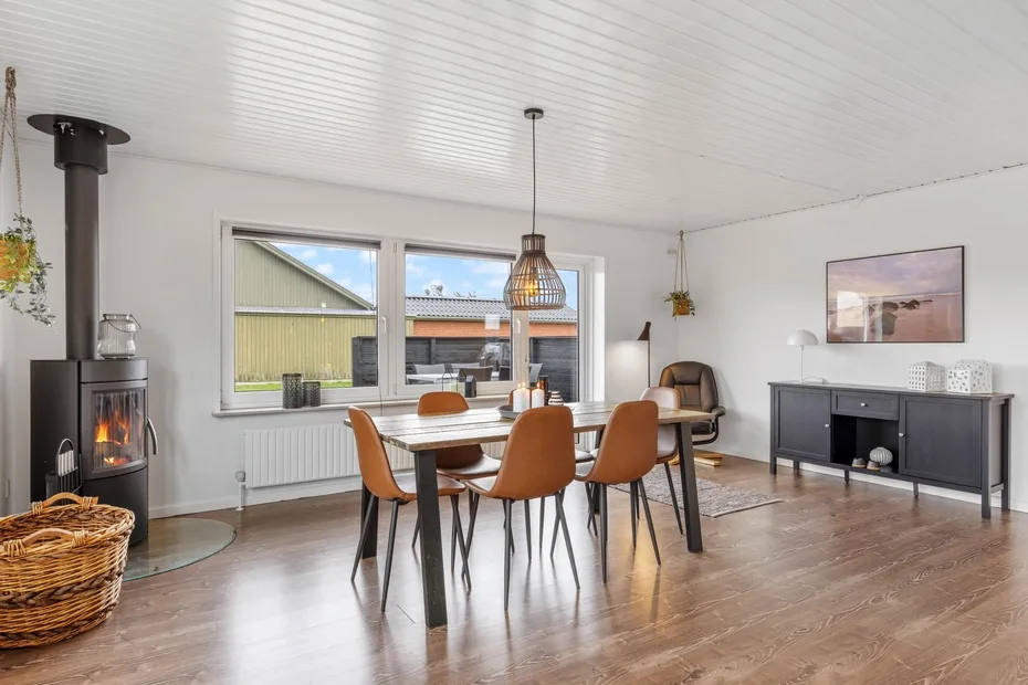 Un comedor luminoso con una mesa de madera y sillas junto a grandes ventanas.