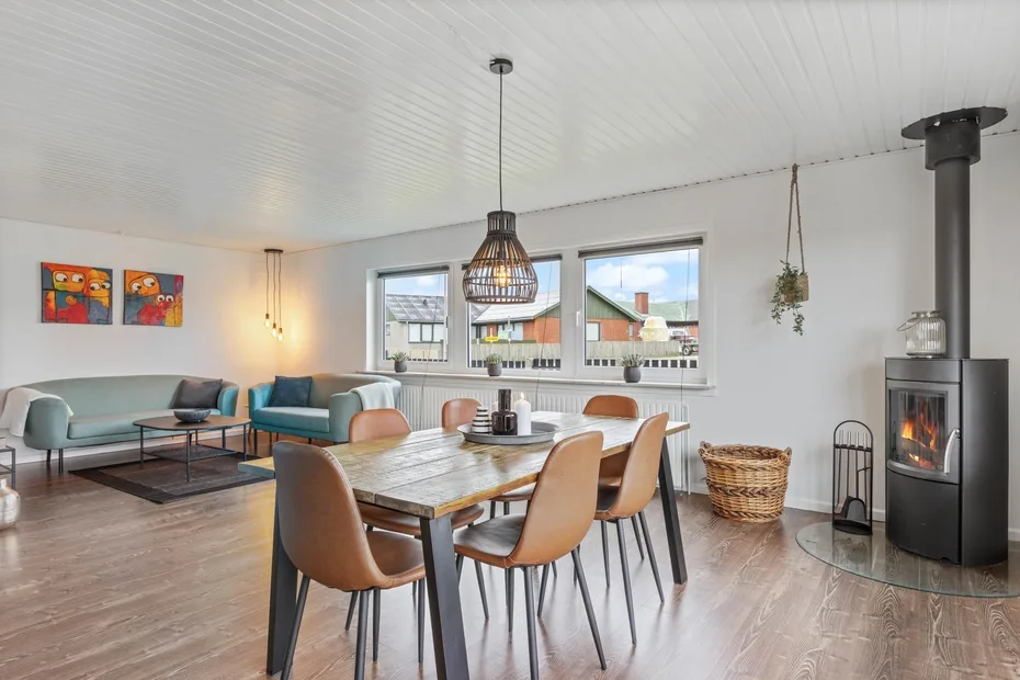 Un comedor junto a una sala de estar, con una mesa de madera y una estufa encendida.