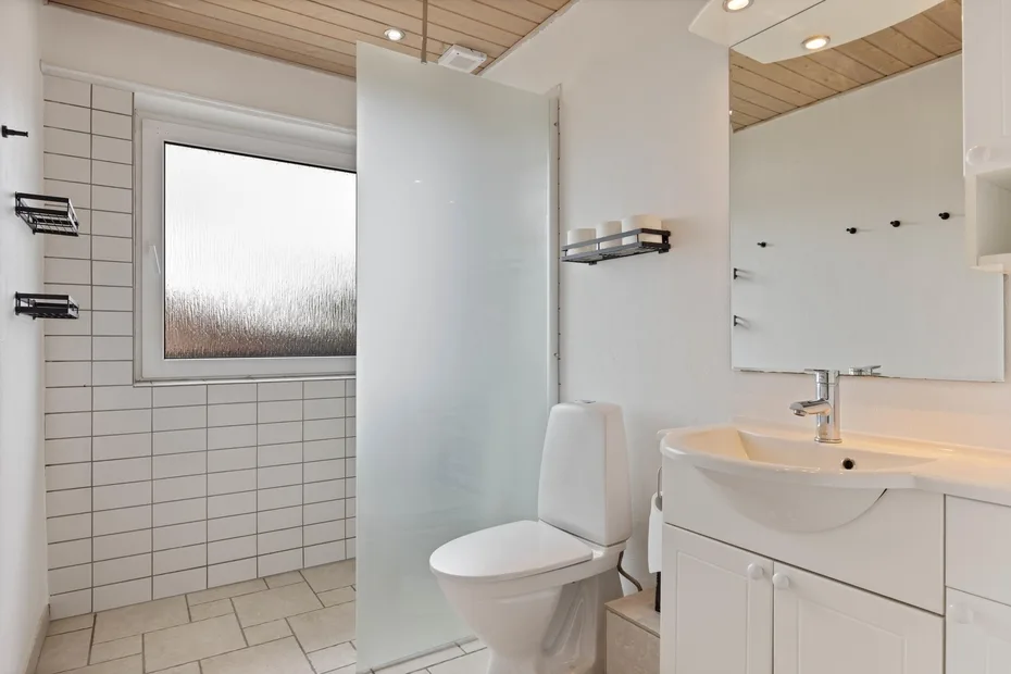 Un baño luminoso con zona de ducha alicatada, inodoro y lavabo con mueble.