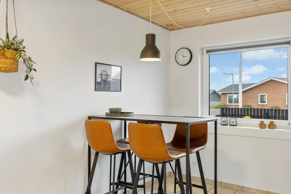 Comedor con una mesa alta y asientos naranjas junto a una ventana amplia.
