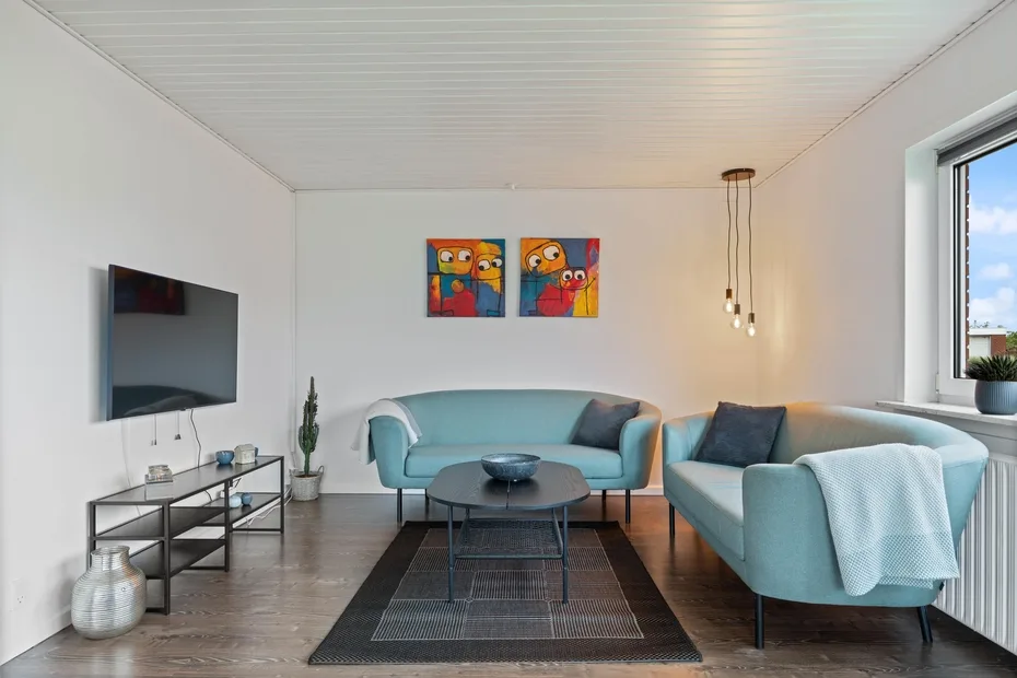 Una sala luminosa con asientos azules, una mesa de centro y arte colorido en la pared.