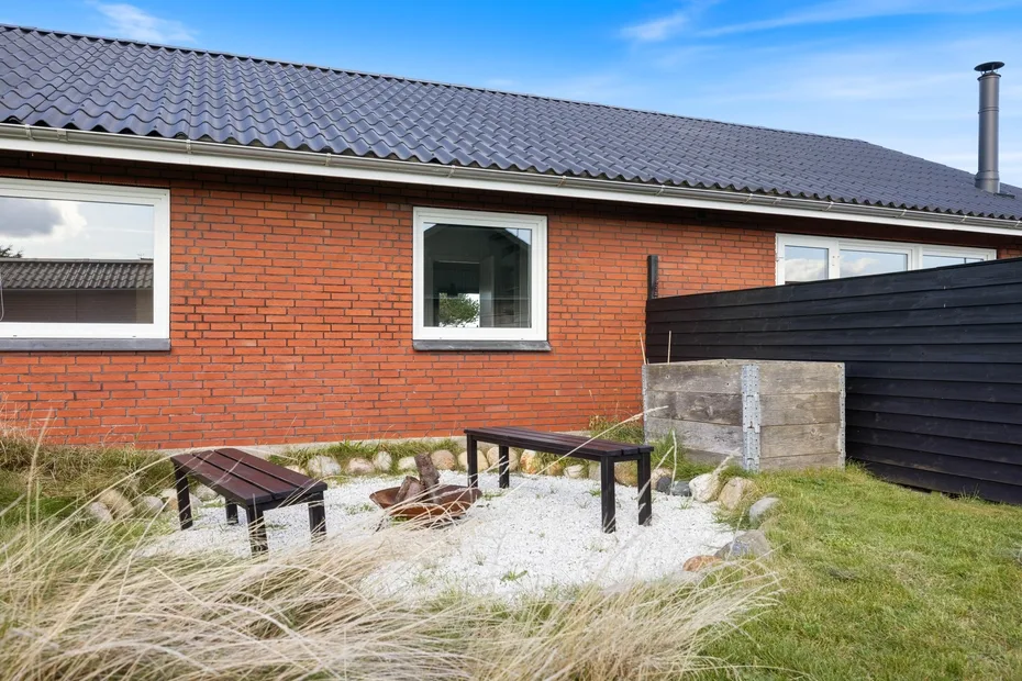 Una casa de ladrillo da a una pequeña zona exterior con mesa y bancos.