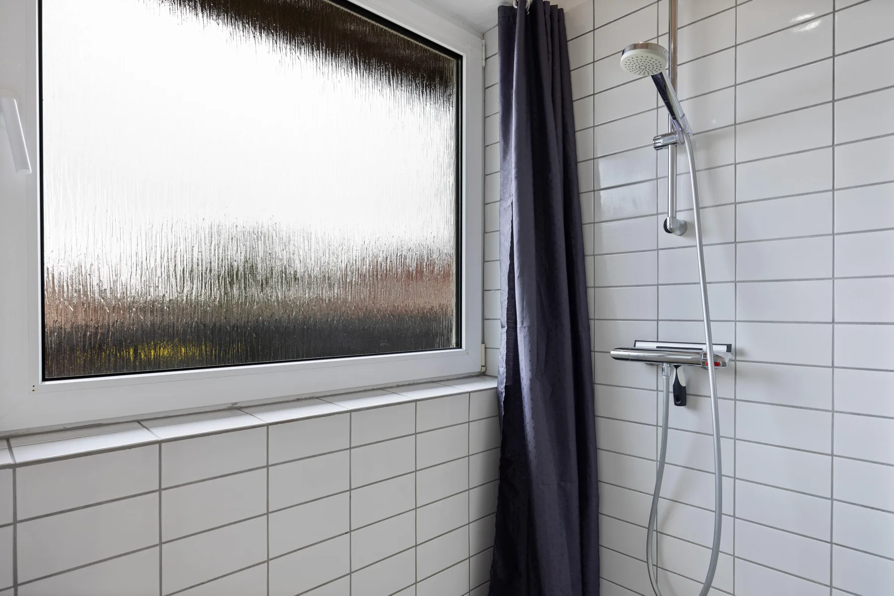 Un baño alicatado con ducha junto a una gran ventana esmerilada.