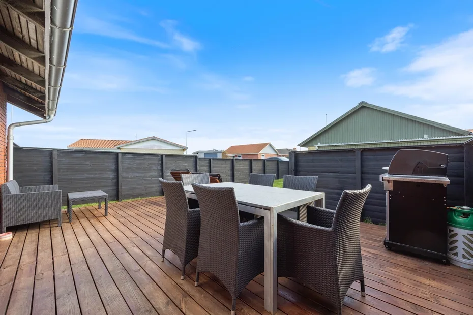 Una terraza de madera tiene una mesa de comedor al aire libre, asientos y una barbacoa.