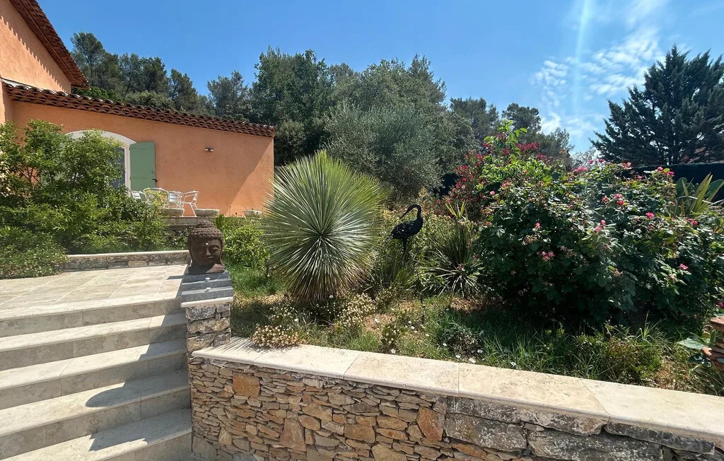 Una terraza ajardinada con escalones de piedra, arbustos floridos y un edificio naranja.