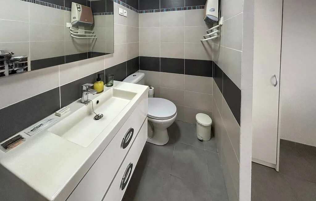 Un baño con azulejos, un largo lavabo, un inodoro y un espejo.
