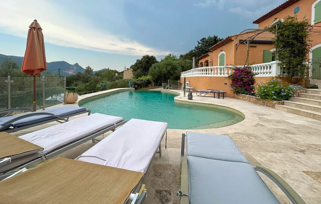 Una piscina al aire libre junto a una casa de color terracota, con tumbonas alrededor.