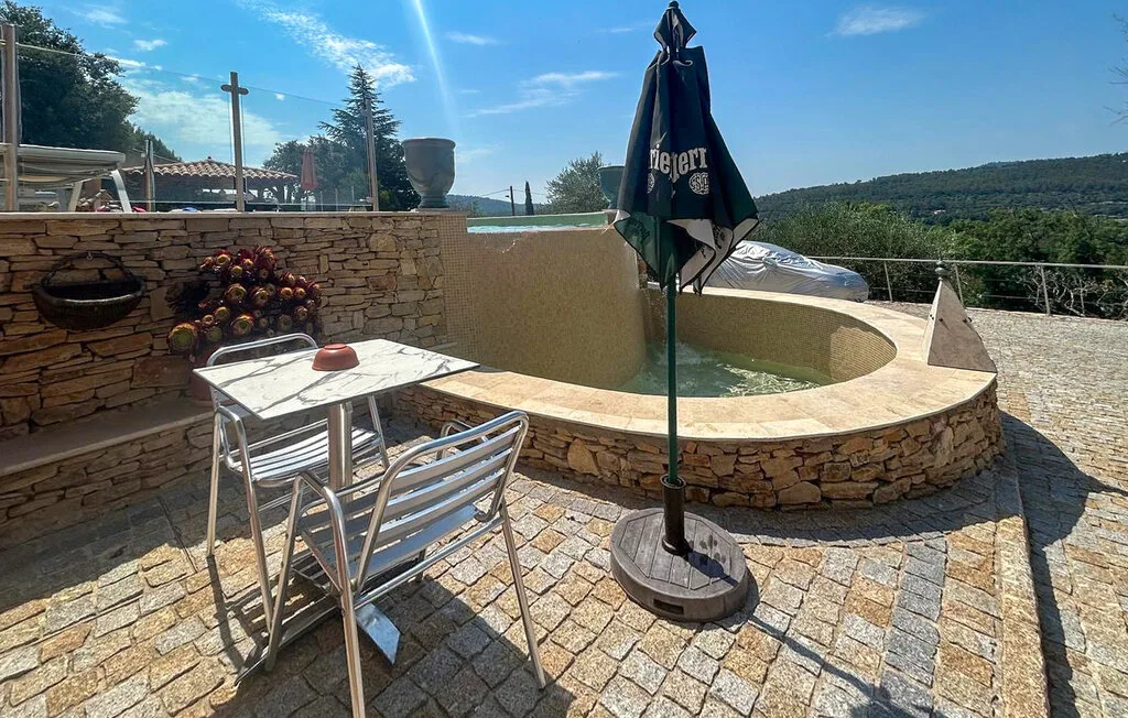 Un patio de piedra con una piscina redonda, asientos al aire libre y una sombrilla cerrada.