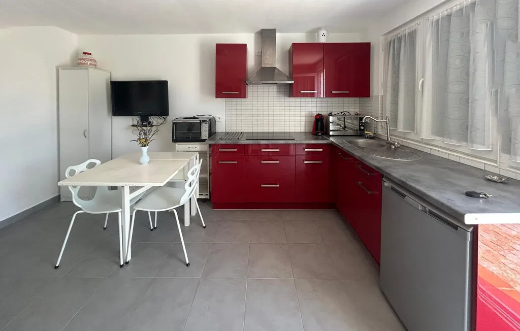 Una cocina con gabinetes rojos, encimeras grises y una mesa de comedor.