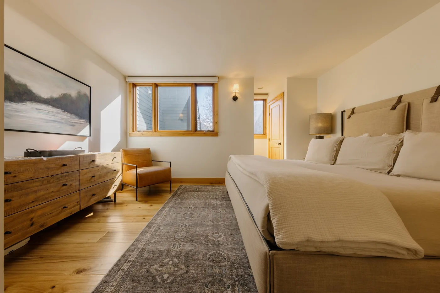 Un dormitorio luminoso con una cama grande, una cómoda de madera y una ventana.