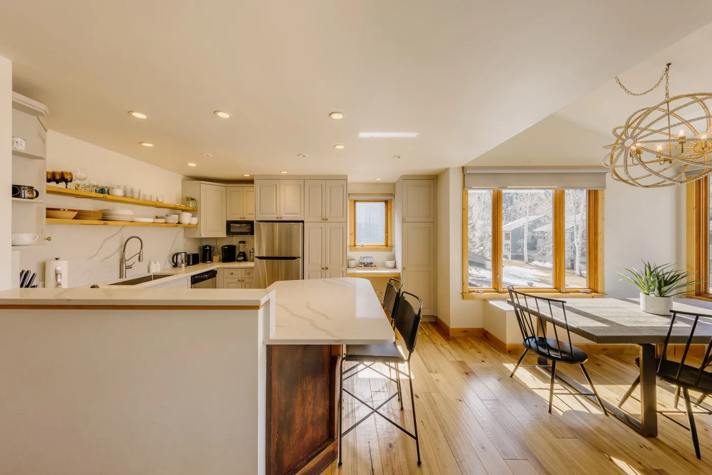 Una cocina abierta y zona de comedor con suelo de madera clara y grandes ventanas.