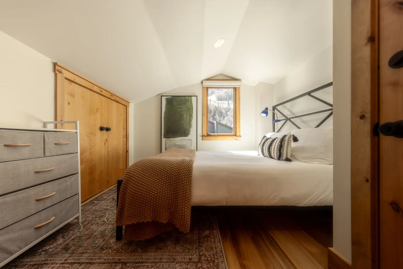 Dormitorio con una cama, un armario de madera y una ventana sobre la cama.