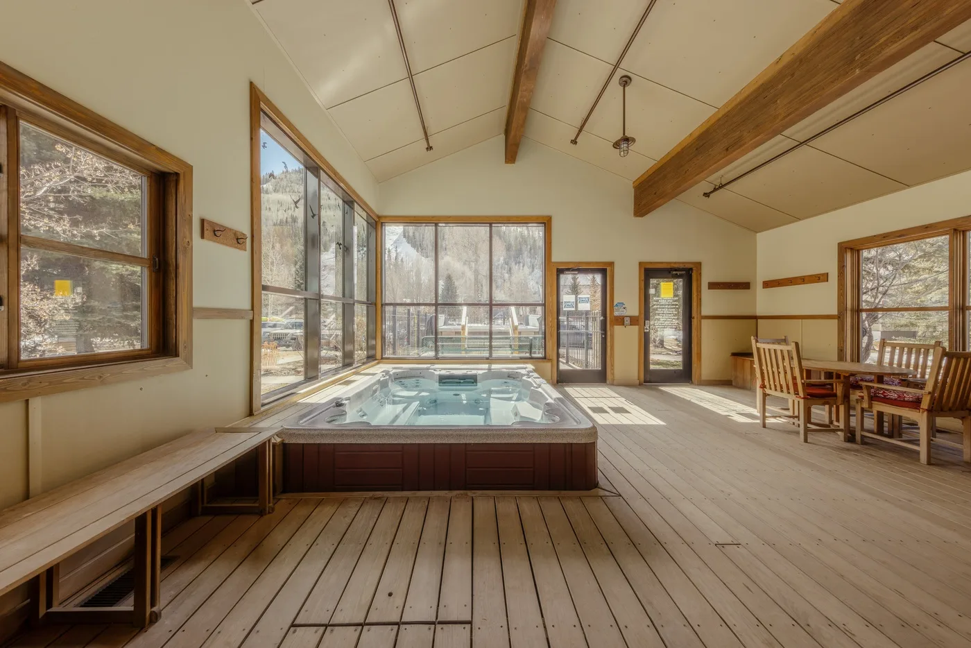 Una luminosa sala de piscina cubierta con grandes ventanas y una terraza de madera.