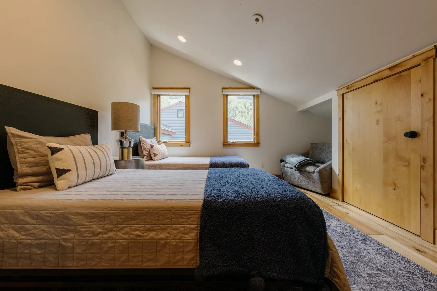 Un dormitorio con una cama, dos ventanas y un armario de madera.