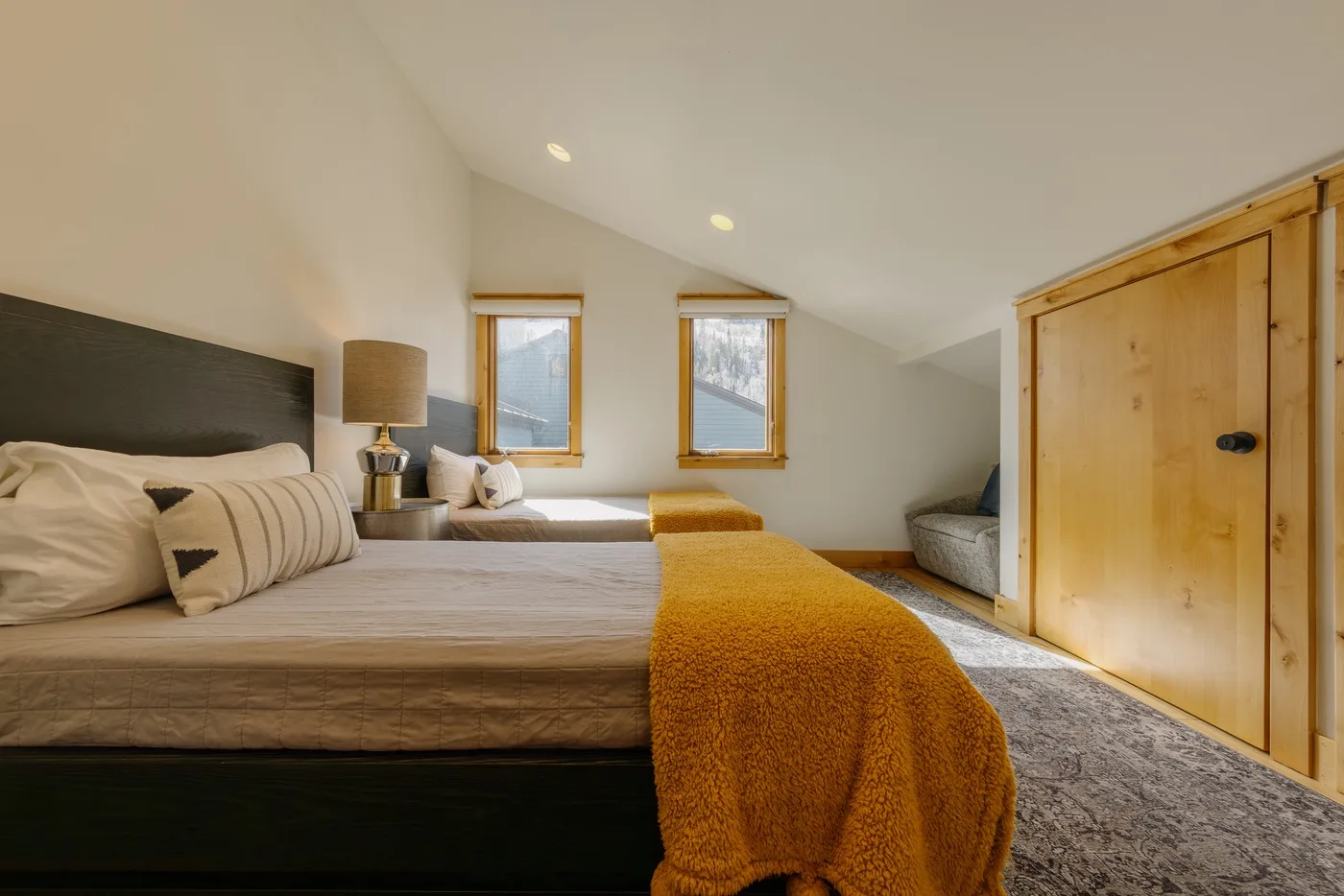Un dormitorio con una cama, dos ventanas y un armario de madera.