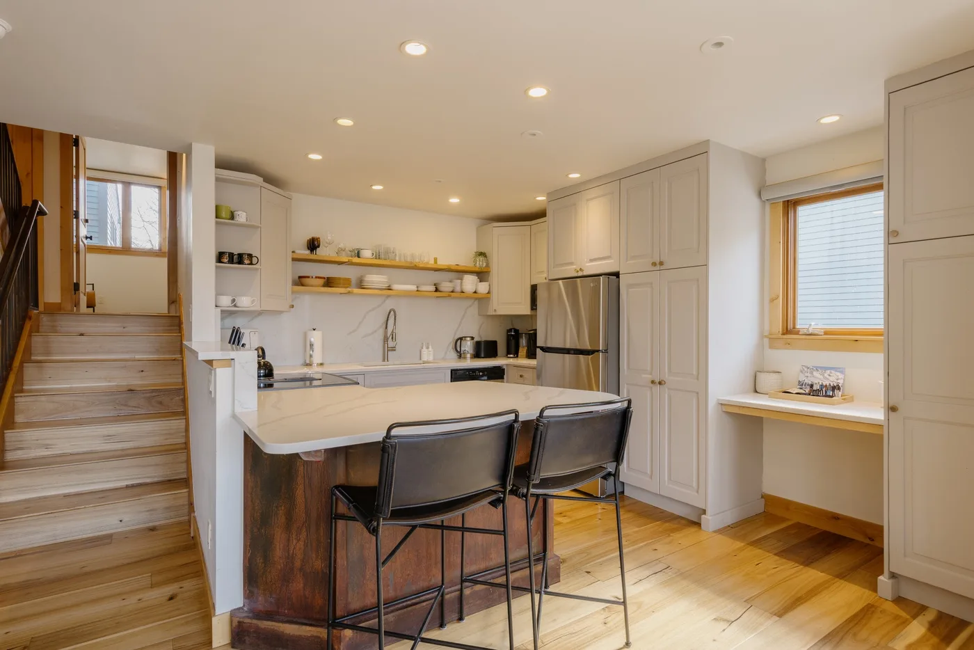 Una cocina luminosa con isla central, asientos de barra y escaleras de madera.