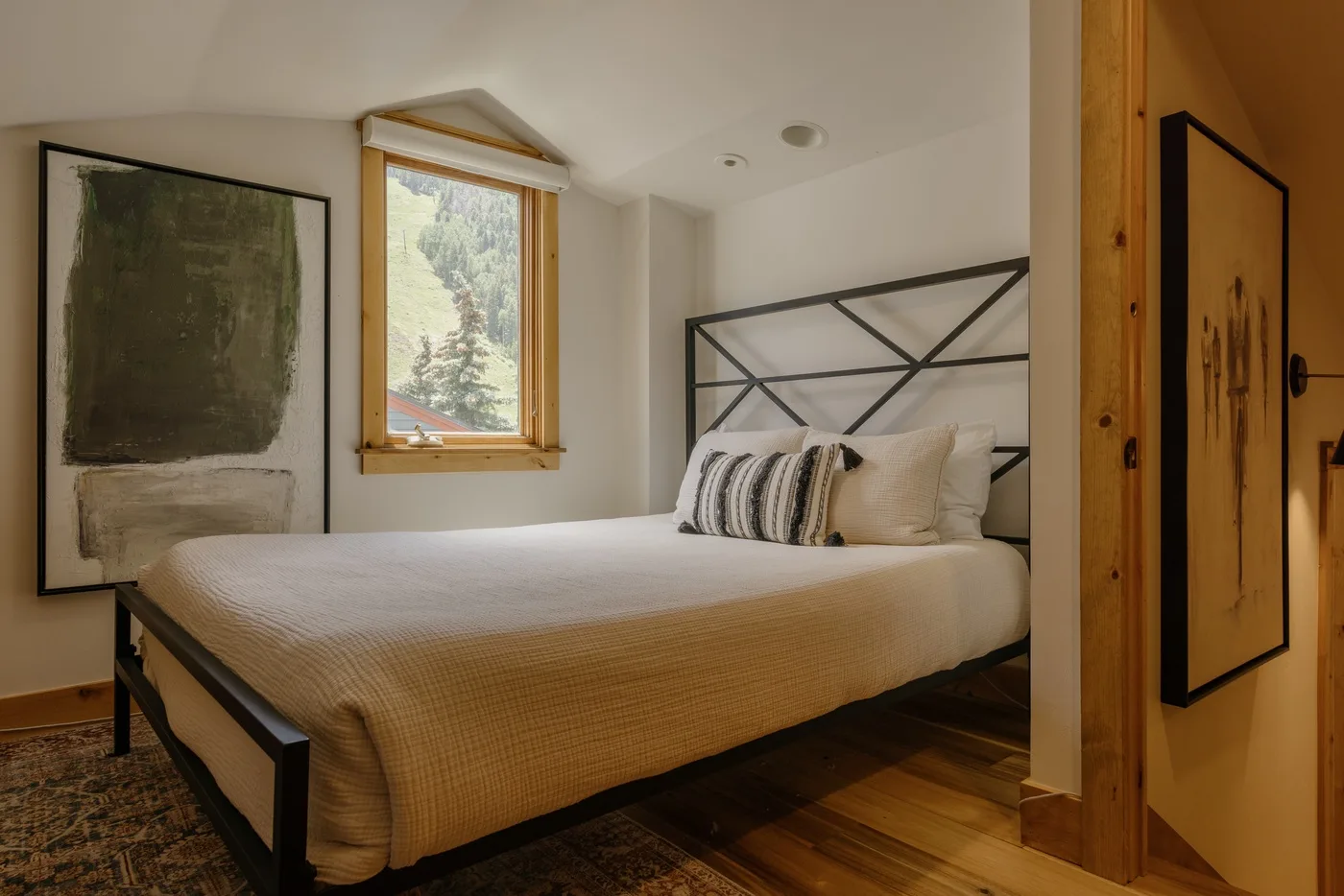 Un dormitorio con una cama junto a una ventana y una obra enmarcada.