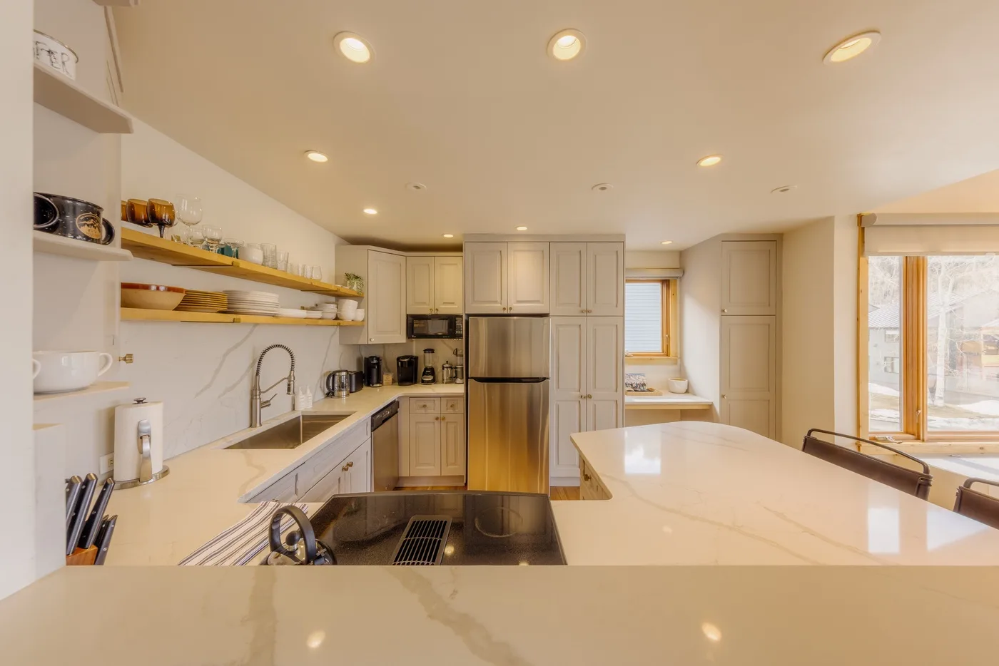 Una cocina luminosa con gabinetes claros, una isla central y electrodomésticos de acero inoxidable.
